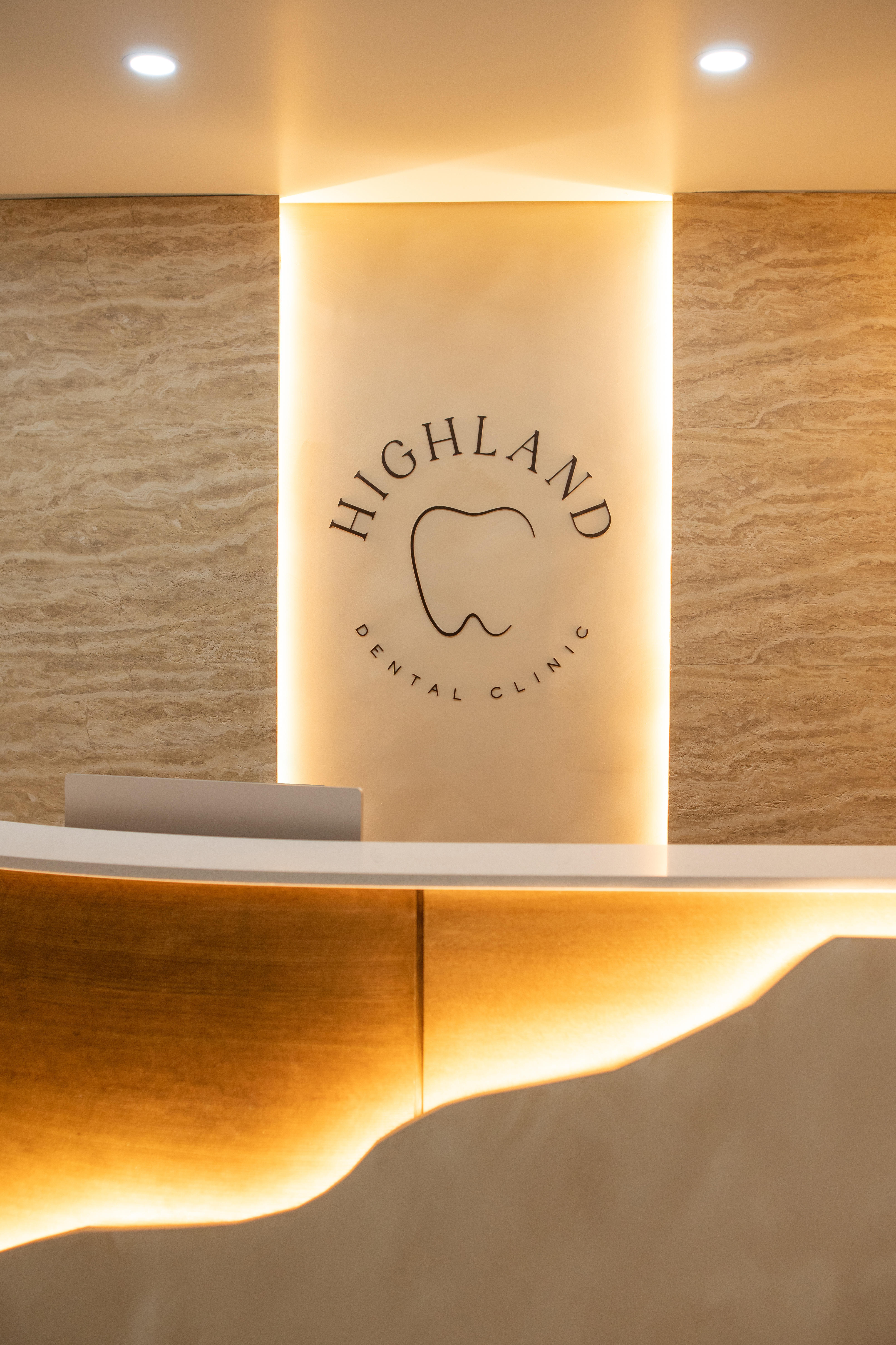 The Allure Dental reception alcove with a backlit travertine niche, sculpted wood front desk, and warm low lighting